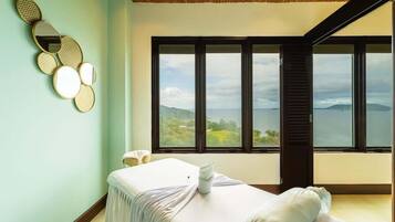 A spa room with a massage table, a wall-mounted mirror, and a large window offering a view of the landscape.