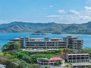 A multi-story hotel with a pool, located near a body of water with hills in the background. - 360 Splendor 306-Condo with Breakfast Included (360 Splendor)