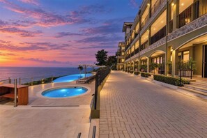 Un hôtel doté d’une piscine, d’un espace extérieur aménagé et offrant une vue sur l’océan au coucher du soleil.