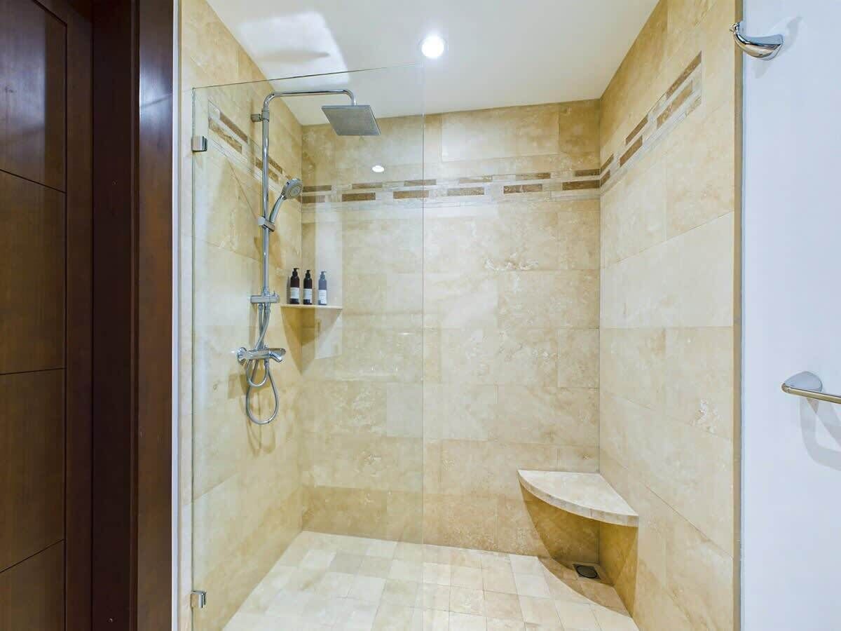 A glass-enclosed shower with a handheld showerhead, a built-in shelf with toiletries, and a small bench.
