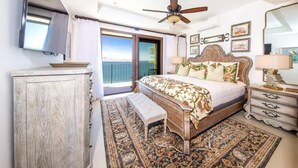 A bedroom with a bed, a ceiling fan, a nightstand, a bench, a dresser, and a large window with curtains. - 360 Splendor 308F- 3 BR Condo, Breakfast Included (360 Splendor)