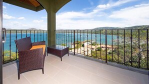 A balcony with a wicker chair and a small table, overlooking a coastal view with mountains and a clear sky. - 360 Splendor 101F-Condo with Breakfast Included (360 Splendor)