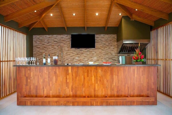 A wooden bar area with a stone wall backdrop, a flat-screen TV, and a kitchen hood.