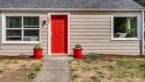 A single-story house with a red door, beige siding, and a grey roof. There are two potted plants on either side of the door. - Remodeled 2 bdrm duplex near the U of O (Eugene)