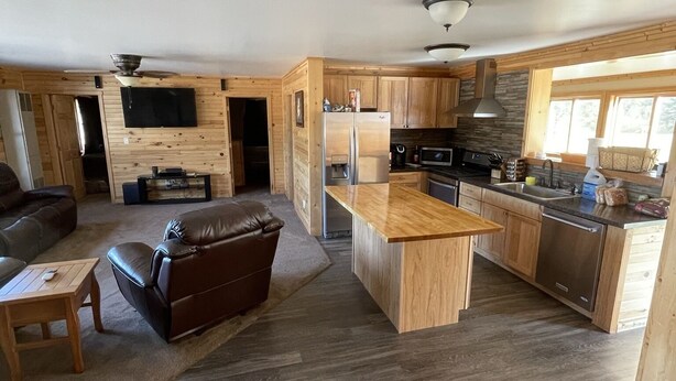 Un vaste espace de vie comprenant un canapé en cuir, une table basse en bois et une cuisine dotée de meubles en bois et d’un îlot central.