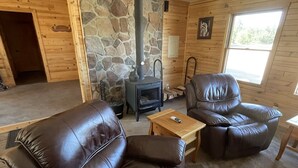 Un salon chaleureux avec un mur en pierre, une cheminée, des fauteuils en cuir et une table en bois.