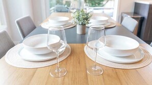 A dining table set with white plates, wine glasses, and a small potted plant. - Modern Home in Walkable Neighborhood, BBQ and Patio! (Portland)