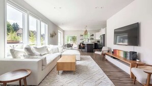 A spacious living area with a sofa set, a coffee table, a TV, and a kitchen in the background. - Modern Home in Walkable Neighborhood, BBQ and Patio! (Portland)
