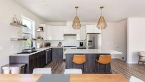 A modern kitchen with dark wood cabinets, a white countertop, and a central island with two chairs. - Modern Home in Walkable Neighborhood, BBQ and Patio! (Portland)