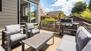 An outdoor deck with a grill, seating area, and sliding glass doors. - Modern Home in Walkable Neighborhood, BBQ and Patio! (Portland)