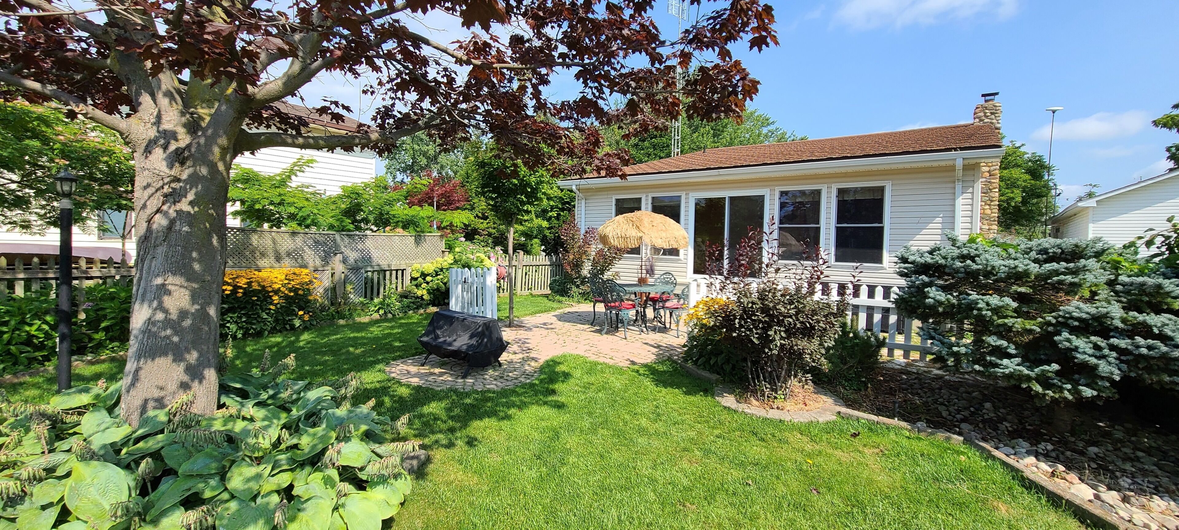 En velholdt baghave med græsplæne, terrassemiljø og et hus med skorsten.