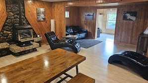 A cozy living room with a stone fireplace, a black leather sofa, a wooden dining table, and a black leather couch.