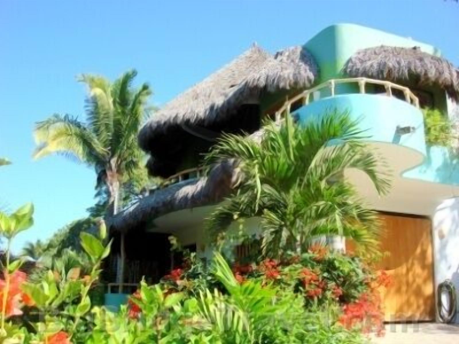 A multi-story building with a thatched roof, surrounded by tropical vegetation and colorful flowers.