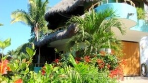 A multi-story building with a thatched roof, surrounded by tropical vegetation and colorful flowers. - Casa Coco  Ocean/Jungle view Studio (Sayulita)