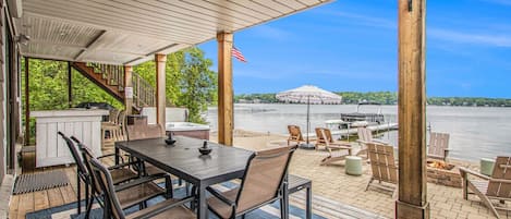 A covered outdoor area with a table and chairs, overlooking a body of water with boats and a dock.