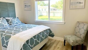 A bedroom with a bed, a window, a chair, and artwork on the walls.