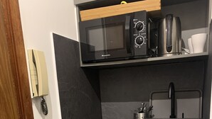 Una cocina compacta con microondas, tostadora y cafetera sobre una encimera negra. Incluye un lavabo con grifo y un armario de madera debajo.