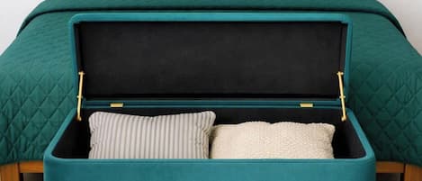 A bed with a teal quilted bedspread, a wooden headboard, and a suitcase with a black interior and teal exterior.