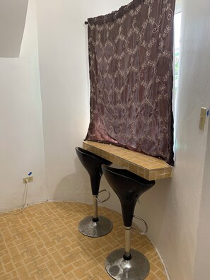 A corner with a brown curtain, a small wooden shelf, and two black bar stools. - Dreams Negril at Coletta's Restaurant - Studio (Negril)