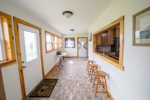 Um corredor estreito com área de cozinha à direita, portas de madeira e uma pequena mesa com cadeiras.
