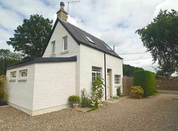 A small, single-story house with a sloped roof, a front door, and a small porch area with potted plants. - Robins Nest Cottage (Blairgowrie)