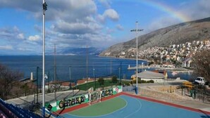Una cancha deportiva al aire libre con vistas a un pueblo costero y una montaña al fondo.