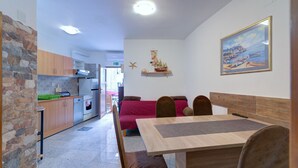 Una cocina moderna con detalles de piedra, un comedor con mesa y sillas de madera, y una zona de estar acogedora con un sofá rojo.