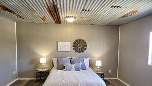 A bedroom with a large bed, two bedside tables, a wall clock, and a ceiling light. - Safari-ish Cabin Getaway in Jacksboro (Jacksboro)