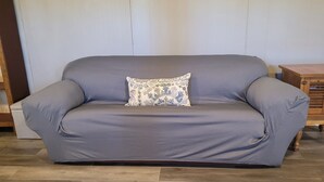 A grey sofa with a patterned pillow in a room with wooden flooring and a wooden side table. - Safari-ish Cabin Getaway in Jacksboro (Jacksboro)