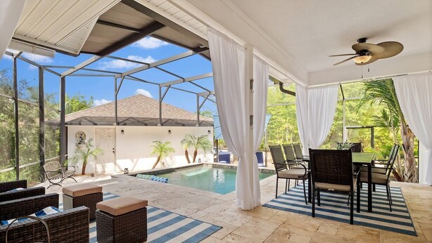 Un espacio al aire libre cubierto con piscina, muebles de mimbre y una mesa con sillas.