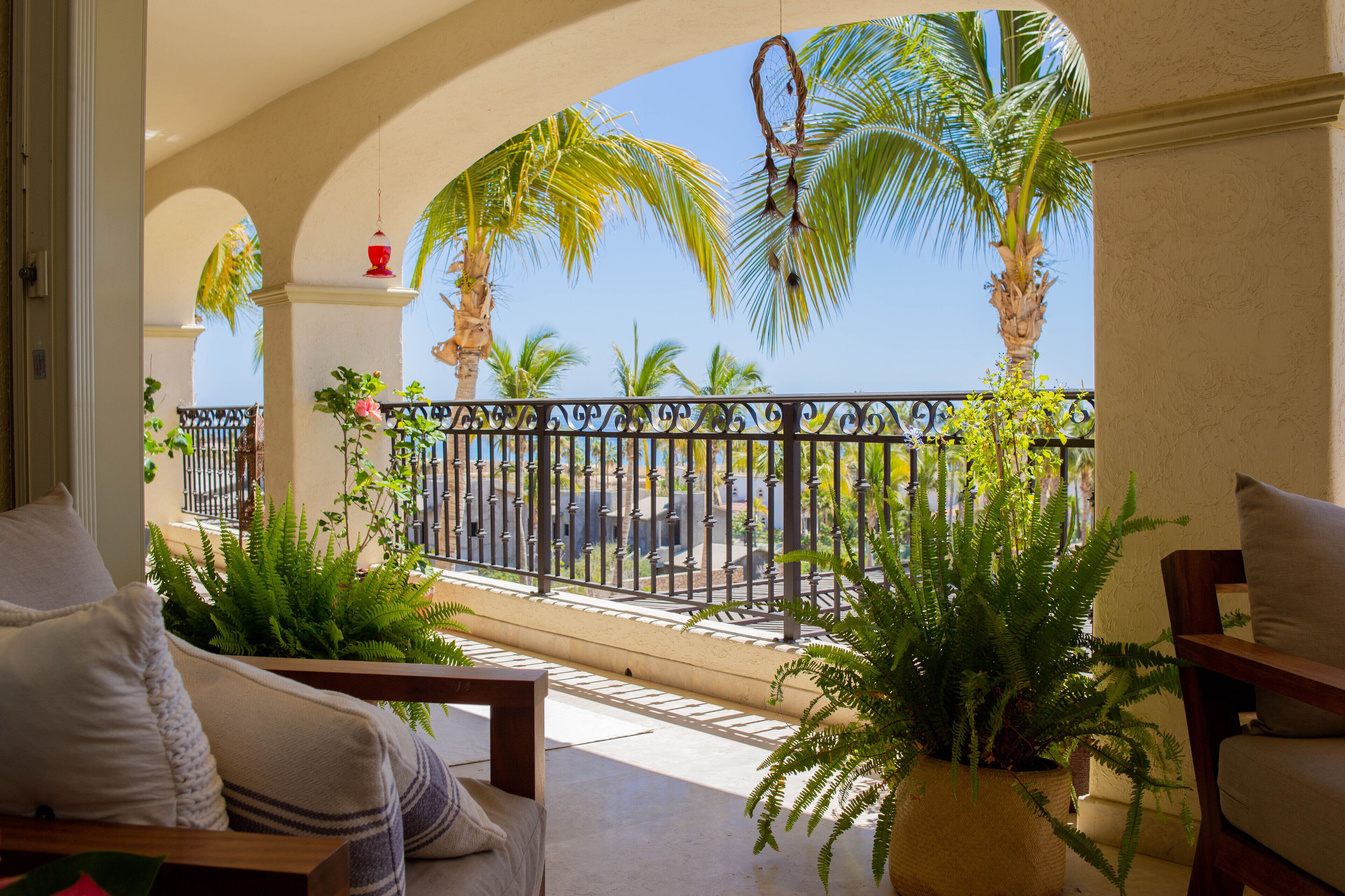 Un balcon avec vue sur des palmiers et une clôture. On y trouve des plantes en pot et une chaise.