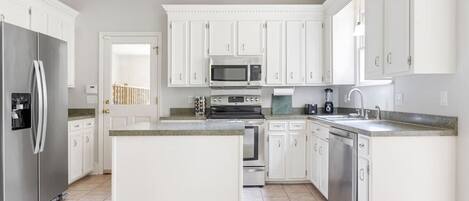 A modern kitchen with white cabinetry, a central island, stainless steel appliances, and a ceiling fan.