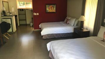 A hotel room with two beds, a desk with a chair, a small kitchenette, and a window with curtains.