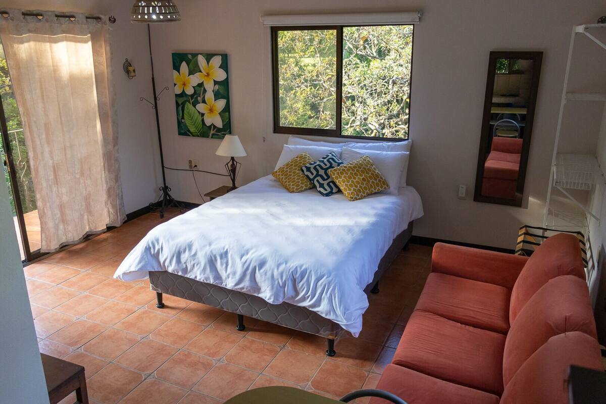 A bedroom with a bed, a window with a view of trees, a chair, and a lamp.