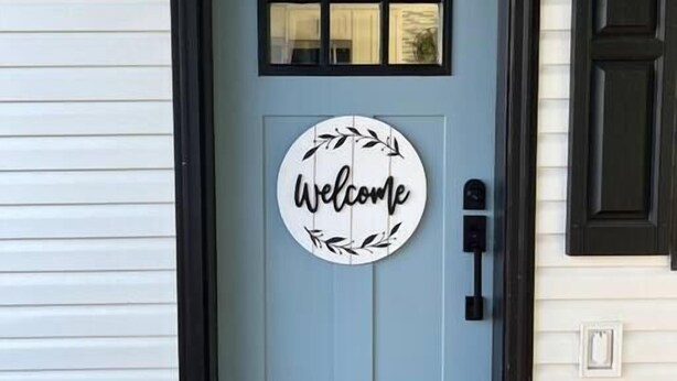 Una puerta principal con un cartel que dice 'Welcome', un buzón y el número 3 encima.