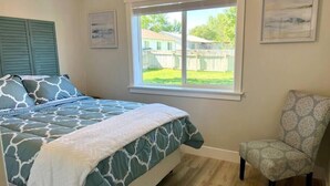 Un dormitorio con cama, una silla, una ventana y vista a un jardín trasero.