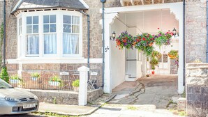 Une maison traditionnelle en pierre, dotée d’une baie vitrée, d’un porche couvert orné de jardinières suspendues et d’une allée pavée.