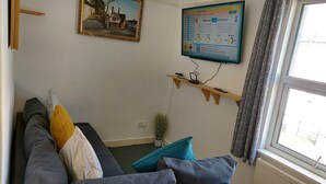 A living room with a sofa, a TV mounted on the wall, a window with curtains, and a small plant. - Victoria Heights - Beautiful 3-bed in Gillingham K (Gillingham)