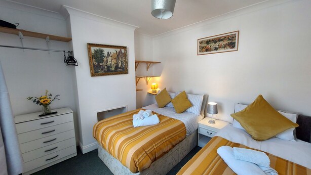 A hotel room with two beds, a wardrobe, a desk, a lamp, and two paintings on the walls. - Victoria Heights - Beautiful 3-bed in Gillingham K (Gillingham)