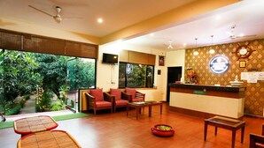 A reception area with a reception desk, seating area with chairs, a small table, and a decorative bowl on the floor. - Corbett Aroma Park By Royal Collection (Ramnagar)
