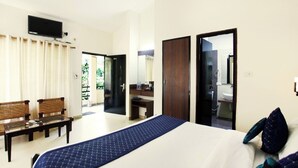 A hotel room with a bed, a desk, a chair, a TV, and a bathroom visible through an open door. - Corbett Aroma Park By Royal Collection (Ramnagar)