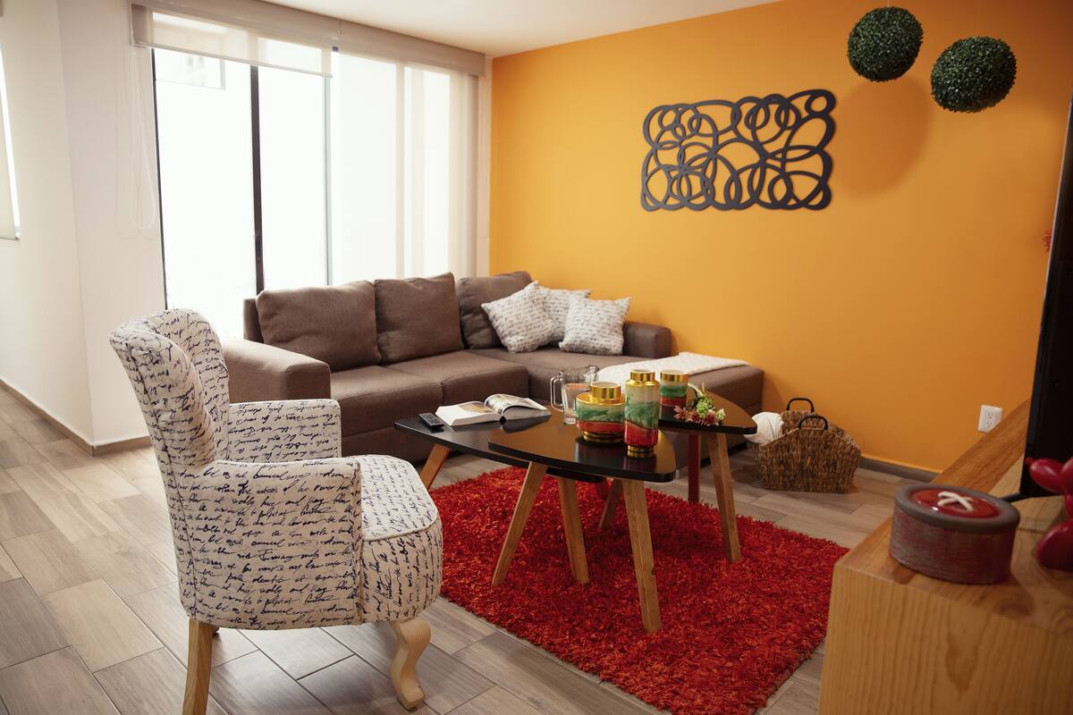 A living room with a brown sofa, patterned armchair, and a glass coffee table with decorative items.