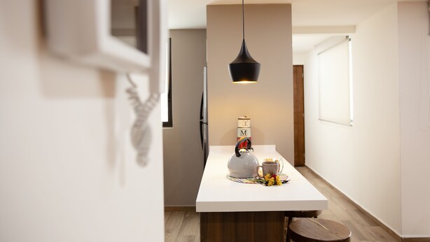A modern kitchen with a white countertop, a kettle, a mug, and a decorative item. - Kolben Nuoma (Mexico City)