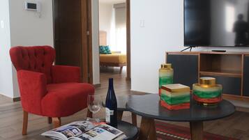 A living room with a red armchair, a round table with a magazine, a wine bottle, and decorative items.