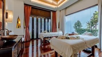 Relax in a serene spa room with a traditional aesthetic, featuring a large window overlooking lush greenery and two massage tables.