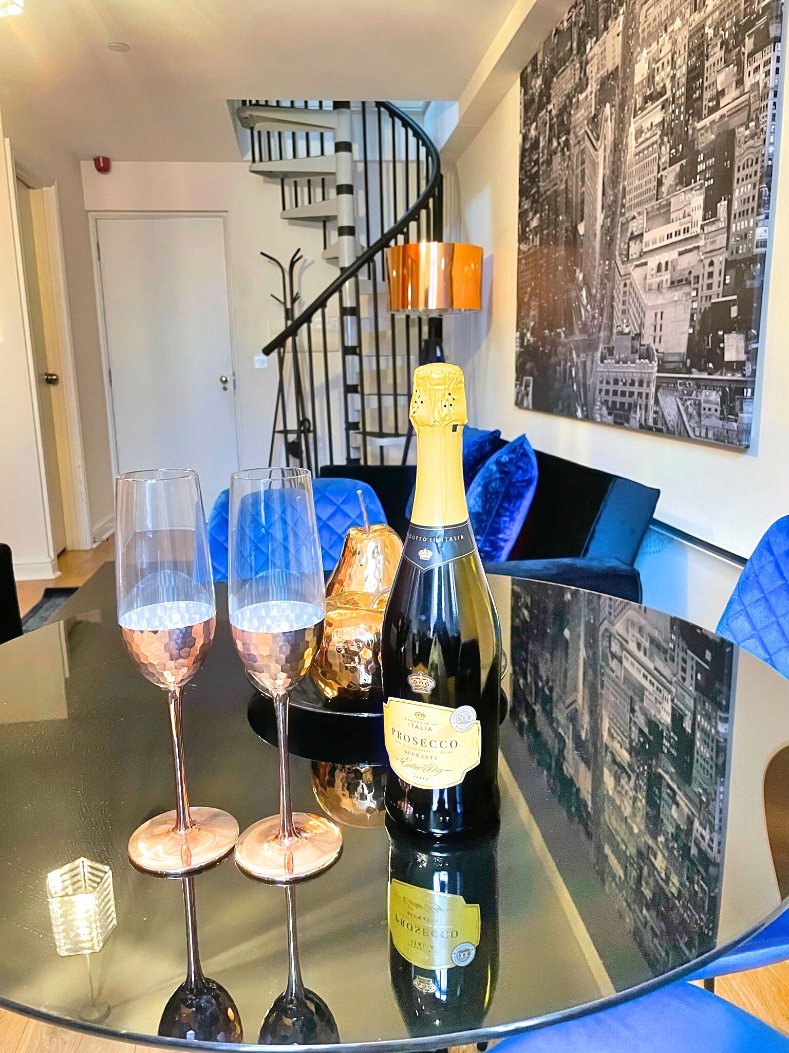 A glass table with three wine glasses and a bottle of Prosecco on a modern glass table.