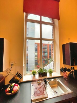 A kitchen with a window, a fruit bowl, a sink, and a plant on the windowsill.
