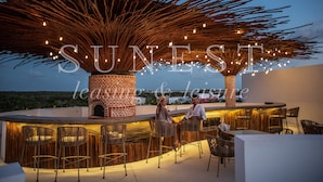 An outdoor bar area with wicker chairs and a brick fireplace, surrounded by a decorative wooden structure with lights. - Hunab Tulum (Tulum)