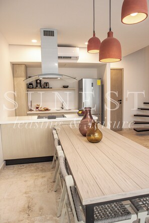 A modern kitchen with a central island, pendant lighting, and a stainless steel refrigerator.
