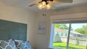 Un dormitorio con cama, ventilador de techo, ventana y vista al jardín trasero.